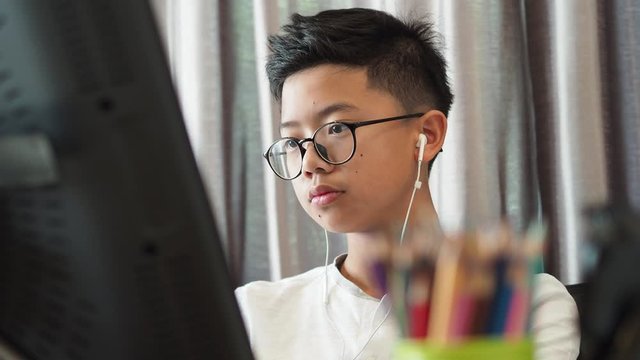 A closeup face of An Asian boy doing online study at his home. He is also wearing an ear phone.