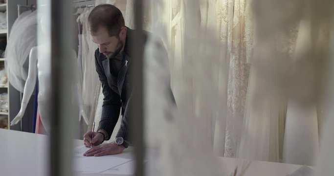 View through the veil of wedding designer draws dress sketch on desk in atelier