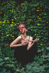 Portrait of beautiful, young, slim and sensual woman in tight black dress and copper mask of Medusa in the forest with yellow flowers at background