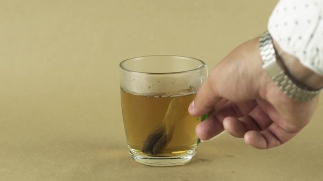 black tea bag lifting and dropping into glass transparent mug to brew tea isolated on beige background slow motion