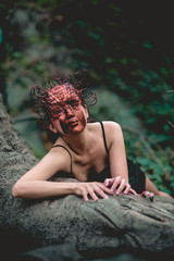 Beautiful, young, slim and sensual woman in tight black dress and copper mask of Medusa in the forest crawling on a tree with little snake