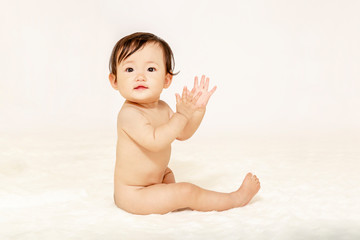 白背景を前に裸で座り手を叩く女の子の赤ちゃん
