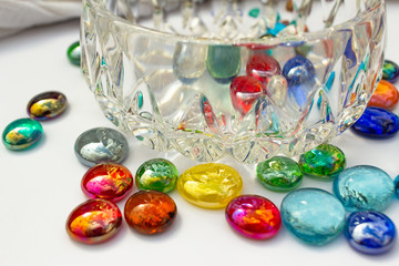 Large modern crystal glass bowl surrounded with multi-color glass drop dragon tears, on white background with copy space