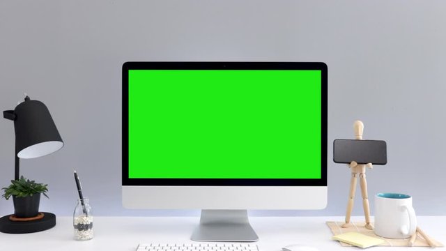 Computer desktop with mock-up green screen with grey background in office and puppet holding a phone black have black lamp on white table, Zoom shoulder view, Chroma Key.