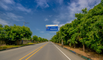 Esmeraldas, Ecuador - March 16, 2016: Paved road in the coast, with informative sign, surrounded with abundat vegetation in a sunny day in the Ecuadorian coasts