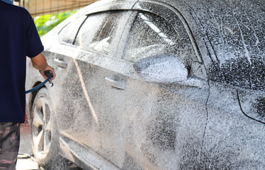 Closeup of black car cleaning, washing with  high pressure foam spraying by male worker's hand. 