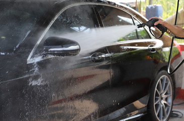 Closeup of black car cleaning, washing by  high pressure water spraying to remove dust and dirty things.