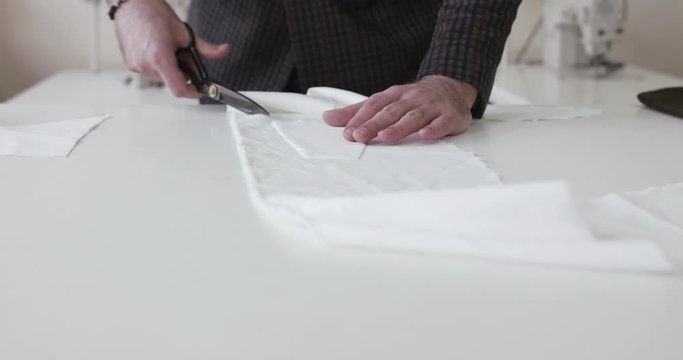 The fashion designer's hands cutting a cloth curve on a desktop in atelier
