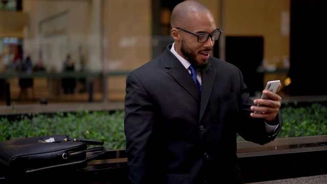 African American trader in classic glasses taking smartphone device for reading received email message with approved information surprised with online opportunity, business concept
