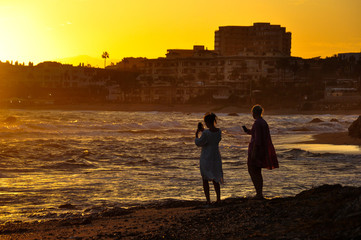 Fototapeta premium Two girls on the beach against the backdrop of the city photograph the sunset