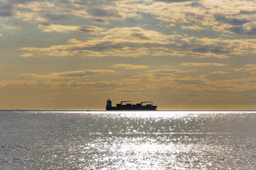 Obraz premium Cargo ship at sea on the horizon photographed contrary the sun