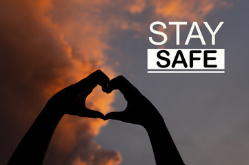 STAY SAFE concept - Female hands in the form of heart against the sky pass sun beams. Hands in shape of love heart