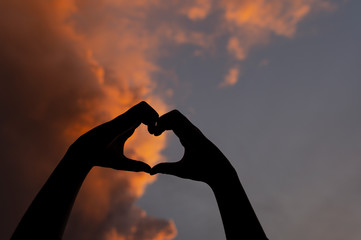 Female hands in the form of heart against the sky pass sun beams. Hands in shape of love heart