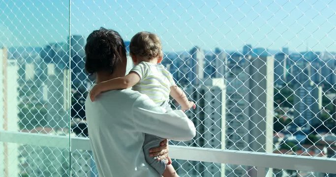 Mom holding baby looking at city view from apartment balcony with safety net