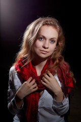 Beautiful gentle girl with long blonde hair in a white shirt and red scarf on dark background. Romantic portrait in calm style