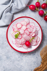 Tasty radish salad in bowl over grey  stone background. Vitamin spring dish from fresh vegetables. Top view, flat lay