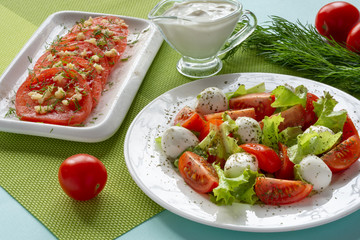 Italian Caprese salad with sliced tomatoes, mozzarella cheese, lettuce leaves, olive oil on a plate. Still-life.
