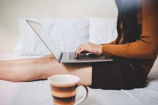 Happy young cassual woman working or shopping online or WFH work from home on laptop while sitting in bed.