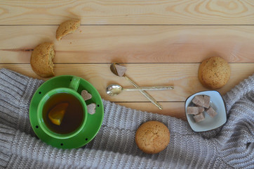 A Cup of lemon tea, a warm sweater, cookies, and heart shaped brown cane sugar on a wooden table. A pleasant tea party in a cozy atmosphere at home