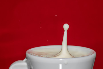 drop of milk falling into a cup with red background