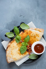 Calzone pizza with fresh green basil leaves over grey concrete background, above view, vertical shot, copyspace
