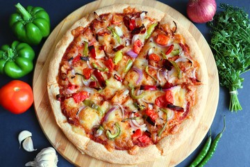 Food- Traditional Italian veggie pizza. Toppings are capsicum, corn, tomatoes, onion, red chilies, and cheese. Ingredients and vegetable background with copy space.