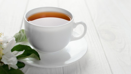 Hot tea in white porcelain cup with white flowers on a branch of apple
on a white wooden background