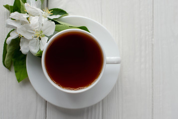Hot tea in white porcelain cup with white flowers on a branch of apple
on a white wooden background