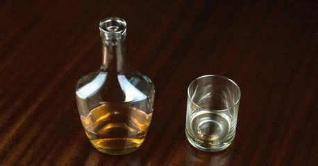 Obraz na płótnie Canvas whiskey bottle near transparent glass reflected on brown wooden table at home closeup