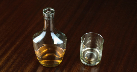 whiskey bottle near transparent glass reflected on brown wooden table at home closeup