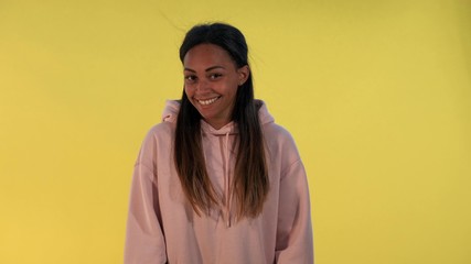 Multiracial girl laughing at somebody. There is yellow background.