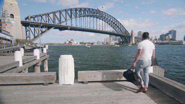 Man Walks in Awe on Wharf by Sydney Harbour Bridge. Tracking Wide Shot