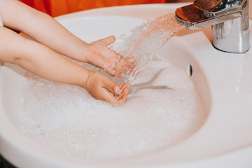 Fototapeta premium Cute little toddler girl washing her hands in a bathroom. Hygiene concept showing prevention of infection and viruses such as flu and covid-19