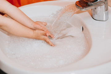 Fototapeta premium Cute little toddler girl washing her hands in a bathroom. Hygiene concept showing prevention of infection and viruses such as flu and covid-19