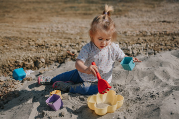 Portrait of little toddler girl playing in the sand with boxes and sand shovel
