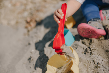Little toddler girl playing in the sand with boxes and sand shovel