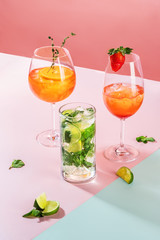  cocktail and mojito cocktail  on pink and blue background with oranges and rosemary