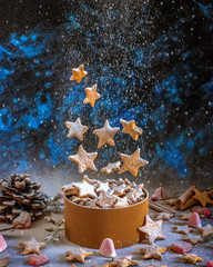 Christmas cookies in the shape of stars that levitate in the air on a Christmas background with sweets and dried fruit in a cloud of icing sugar