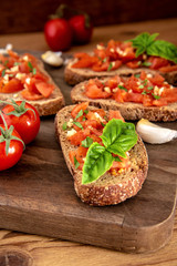 Garlic bread with fresh tomatoes and basil in the foreground on rustic wooden table