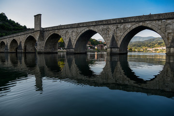 Fototapeta na wymiar The Ottoman Mehmed Pasa Sokolovic Bridge over Drina river in Visegrad, Bosnian mountains, with fantastic sky scape and river reflection. Bosnia and Herzegovina.
