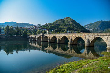 Fototapeta na wymiar The Ottoman Mehmed Pasa Sokolovic Bridge in Visegrad, Bosnian mountains, with fantastic sky scape and river reflection. Bosnia and Herzegovina..