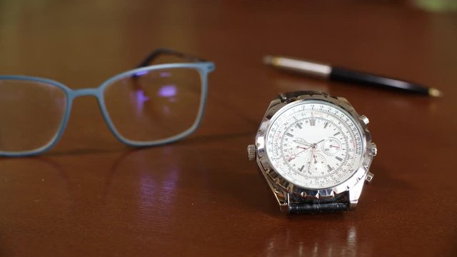 Close up view of wrist watch and eyeglasses on table. Wrist watch ticking. Procrastination and time management concept. The time is money