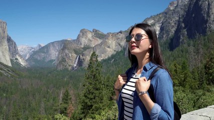 asian young travel woman standing with hand carry backpack on mountain valley looking at panoramic view of bridal veil fall in yosemite. beautiful girl traveler enjoy sunshine outdoor in nature.