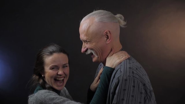 furious woman with dark braid holds aged grey haired man ears and pulls angrily in professional studio close view. People emotion