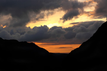 Clouds building at sunset above a valley, with a silhouette of mountains either side