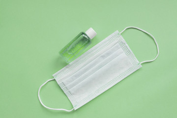 medical mask and sanitizer on green background. Stay home hygienic quarantine concept. Flat lay, top view