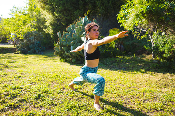 The girl practices yoga on the green grass on a background of green trees.