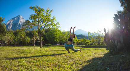 Fototapeta na wymiar The girl practices yoga on the green grass on a background of green trees and mountains.
