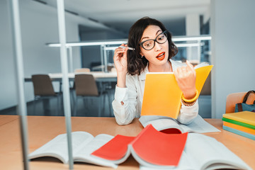 Thoughtful Asian girl a student or PhD professor reads books and lectures in a modern library in university campus