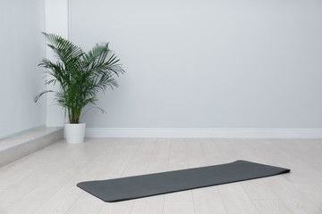 Unrolled black yoga mat on floor in room. Space for text - obrazy, fototapety, plakaty